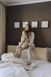 Frau mit Tochter sitzt auf Kopfteil im Schlafzimmer zu Hause - SEAF00624