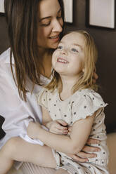 Smiling woman sitting with cute daughter at home - SEAF00625