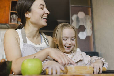 Cheerful mother with daughter holding rolling pin in kitchen - SEAF00636