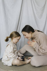 Lächelnde Frau im Gespräch mit ihrer Tochter, die zu Hause eine Kamera hält - SEAF00650