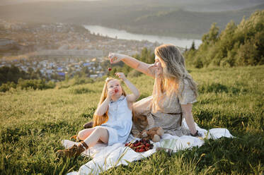 Happy mother feeding berries to daughter sitting on grass - VBUF00034