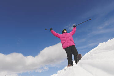 Mann mit erhobenen Armen und Skistöcken im Schnee stehend - OMIF00708