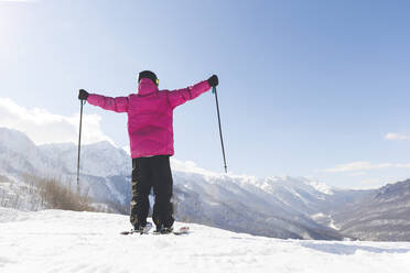 Mann mit Skistöcken stehend mit ausgestreckten Armen im Winter an einem sonnigen Tag - OMIF00724