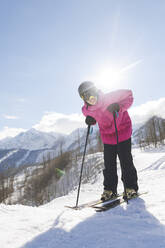 Lächelnder Mann, der sich im Winter an einem sonnigen Tag über Skistöcke beugt - OMIF00725