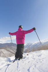 Mann mit Skistöcken stehend mit ausgestreckten Armen im Winter an einem sonnigen Tag - OMIF00728