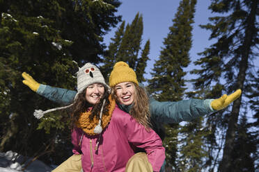 Happy woman carrying friend with arms outstretched enjoying in winter forest - VBUF00047