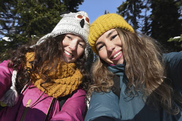 Lächelnde Frauen mit braunen Haaren tragen Strickmütze im Winter an einem sonnigen Tag - VBUF00049