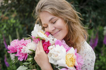Lächelnde blonde Frau mit geschlossenen Augen umarmt Blumen - VBUF00053