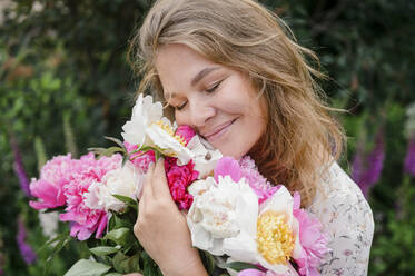 Smiling blond woman with eyes closed hugging flowers - VBUF00053