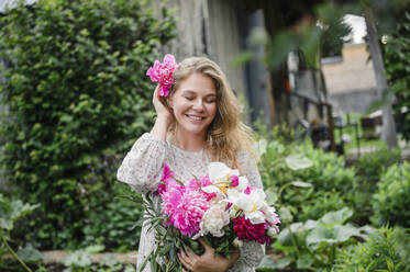 Schöne lächelnde blonde Frau mit rosa Blume steht im Garten - VBUF00056