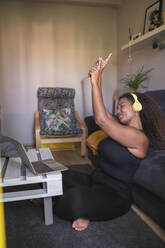 Young woman with arms raised listening music through wireless headphones in living room - SNF01587