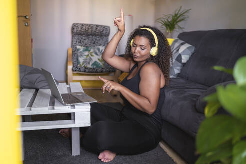 Woman listening music through wireless headphones enjoying in living room at home - SNF01588