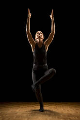 Frau mit erhobenem Arm übt Yoga vor schwarzem Hintergrund - STSF03144