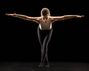 Woman with arms outstretched doing yoga against black background - STSF03146