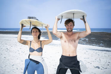 Glückliches Paar mit Surfbrett am Strand an einem sonnigen Tag - FBAF01834