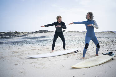 Man teaching woman surfing lesson on beach - FBAF01838