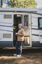 Älterer Mann mit Kaffeetasse vor der Tür eines Wohnmobils - SIPF02790