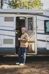 Senior man with coffee cup standing at door of motor home - SIPF02790