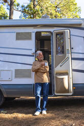 Älterer Mann mit Kaffeetasse vor der Tür eines Wohnmobils - SIPF02791