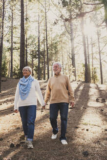 Happy senior couple in warm clothing walking together in forest - SIPF02800