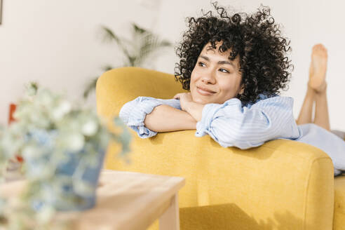 Smiling thoughtful woman lying on sofa in living room at home - XLGF02815