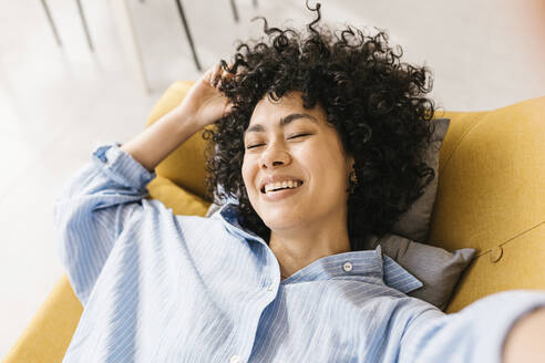 Happy young woman with eyes closed lying on sofa at home - XLGF02830