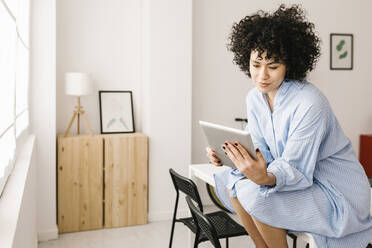 Junge Frau mit Tablet-PC sitzt auf dem Tisch im Wohnzimmer zu Hause - XLGF02832