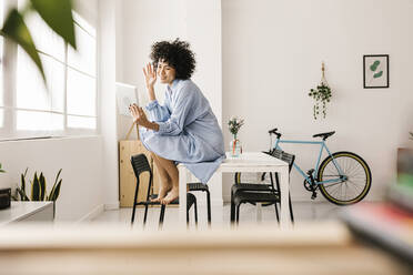 Smiling woman waving hand on video call through tablet PC sitting on table at home - XLGF02834