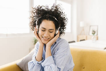 Happy young woman enjoying music through wireless headphones at home - XLGF02848