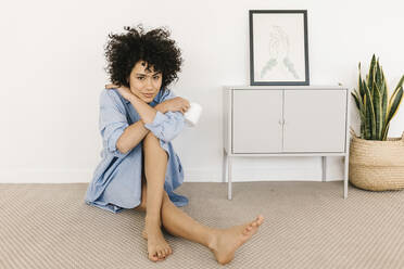 Lächelnde junge Frau mit Kaffeetasse sitzt auf dem Boden durch weiße Wand zu Hause - XLGF02852