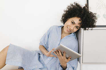 Glückliche junge Frau mit Tablet-PC, die sich zu Hause auf einen Schrank stützt - XLGF02858