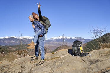 Man carrying girlfriend gesturing peace sign on sunny day - VEGF05324