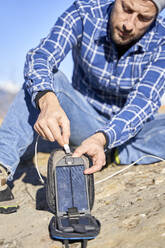 Mann lädt sein Smartphone an einem sonnigen Tag mit einem tragbaren Solarmodul auf - VEGF05328