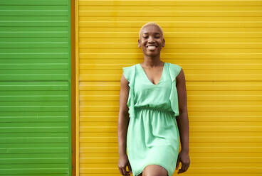 Happy young woman standing in front of green and yellow wall - VEGF05334