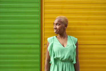 Junge Frau mit kurzen blonden Haaren steht vor einer grün-gelben Wand - VEGF05338