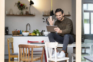 Happy freelancer waving hand on video call through tablet PC in kitchen at home - PESF03440