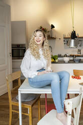 Fröhliche blonde Frau mit Kaffeetasse auf dem Tisch in der Küche zu Hause - PESF03466