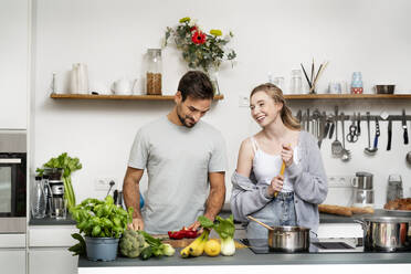 Happy woman standing by boyfriend chopping food in kitchen at home - PESF03474