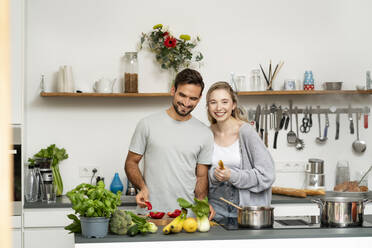 Happy girlfriend and boyfriend preparing food in kitchen - PESF03476