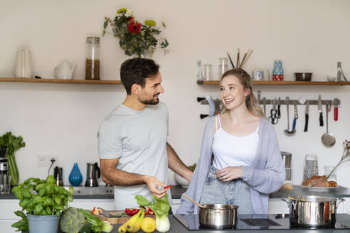 Lächelnder junger Mann und Frau unterhalten sich in der Küche zu Hause - PESF03478