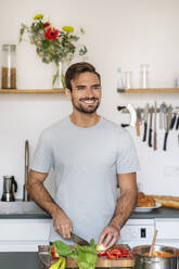 Lächelnder gutaussehender Mann, der in der Küche zu Hause Essen hackt - PESF03482