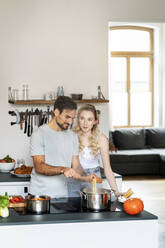 Blonde Frau im Gespräch mit ihrem Freund bei der Herstellung von Nudeln in der Küche zu Hause - PESF03485