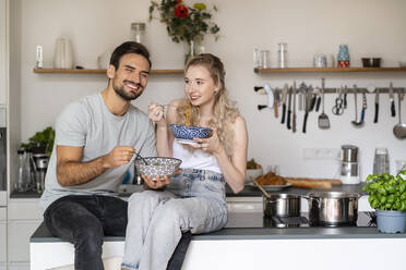 Lächelnde junge Frau und Mann essen Spaghetti auf der Kücheninsel zu Hause - PESF03490