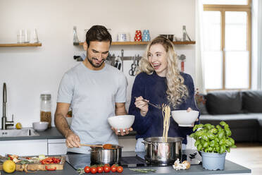 Glückliche Frau, die Spaghetti serviert, steht neben ihrem Freund in der Küche - PESF03495