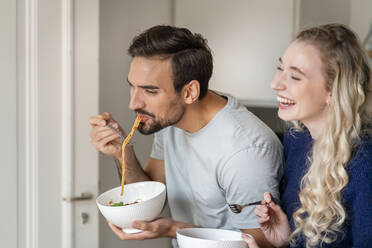 Glücklicher junger Mann isst Spaghetti mit einer fröhlichen Freundin zu Hause - PESF03497