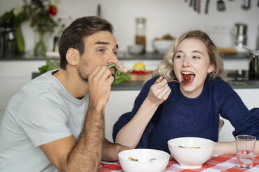 Young woman and man eating food sitting at table - PESF03498