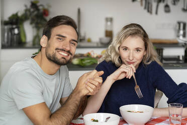 Smiling young man with blond girlfriend sitting at table - PESF03500