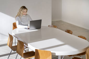 Smiling young woman using laptop sitting at table - PESF03527