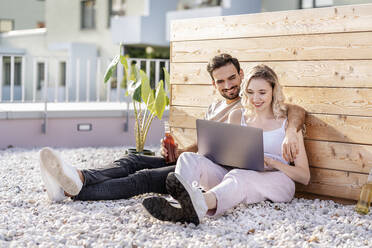 Smiling young couple sharing laptop on sunny day - PESF03536