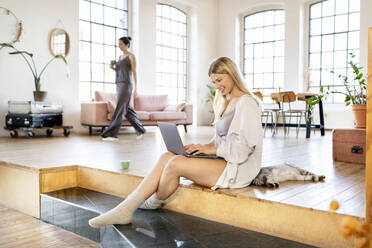 Smiling businesswoman using laptop sitting by pet cat at home - DMOF00189